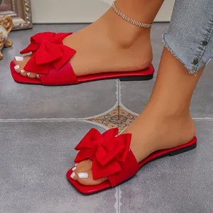 Detailed view of vibrant red flat sandals featuring a large decorative bow on square toe.