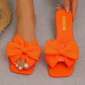 Close-up of vibrant orange flat slides featuring a large, textured fabric bow detail