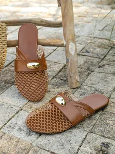 Detail of brown mesh flat mules with a stylish metallic oval buckle on stone pavement.