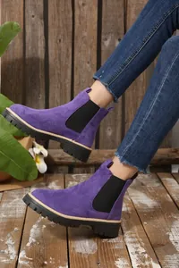 Primo piano di stivaletti Chelsea in pelle scamosciata viola con suola spessa nera.
