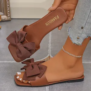 Close-up of brown flat sandals with a large fabric bow and golden lettering