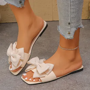 Close-up view of women's beige flat sandals featuring a large textured bow detail.