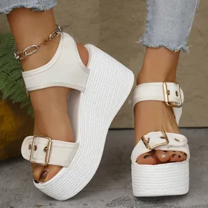 Close-up detail of white wedge platform sandals with straw woven heel and gold buckles.