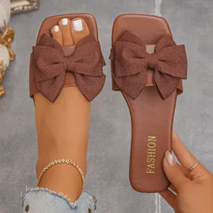 Detailed macro view of women's brown flat sandals featuring an elegant oversized fabric bow