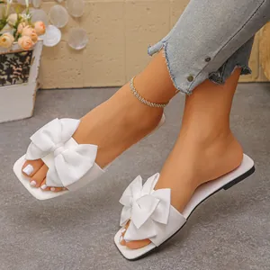Close-up view of stylish white flat slide sandals featuring an elegant large bow detail