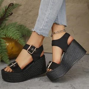 Detailed view of black platform wedge sandals with gold buckles and braided straw texture.