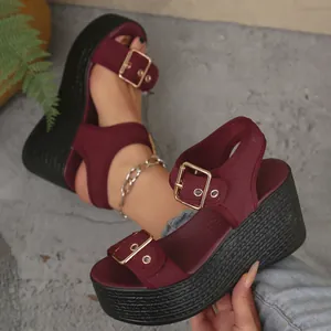 Detail view of burgundy wedge sandals with elegant gold buckles and a woven black platform sole
