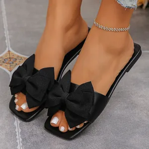 Close-up of elegant black flat sandals with large bow decoration on feet
