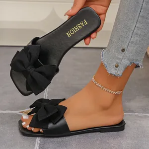 Close-up view of black flat slide sandals with a large decorative bow and gold fashion logo.