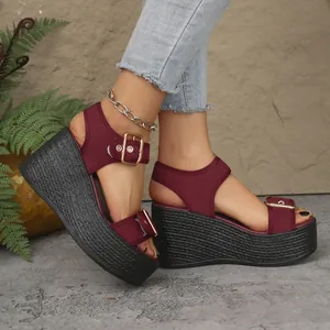 Detail of burgundy wedge sandals with black straw-weave soles and gold buckle accents.