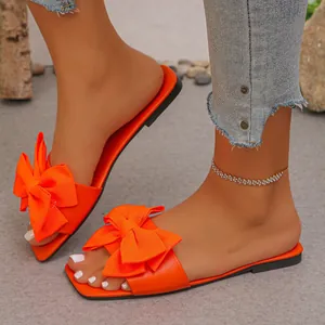 Close-up detail of vibrant orange flat sandals featuring a stylish large bow knot.