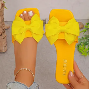 Vibrant yellow women's flat slide sandals with oversized bow detail, close-up view.