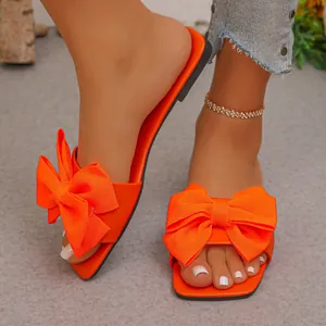 Close-up view of bright orange flat slippers featuring large textured decorative bows