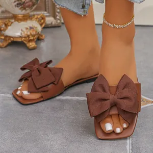 Close-up of brown flat slide sandals for women with elegant oversized bow decoration