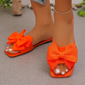 Close-up of vibrant orange flat sandals featuring a large textured fabric bow