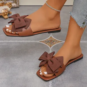 Stylish brown flat sandals for women featuring a large decorative bow and square toe design