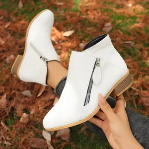 Close-up view of white suede ankle boots featuring a side zipper and wood-grain block heel.