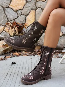 Detailed side view of brown mid-calf boots with floral embroidery and lace-up design.