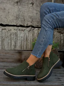 Detailed view of dark green suede ankle boots with side zipper and lug sole on feet