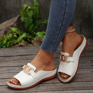 Detail of white wedge sandals with gold buckle shown on model in outdoor setting