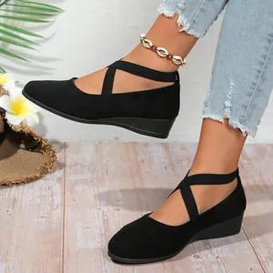 Black faux suede wedge shoes with crisscross elastic ankle straps on wooden floor
