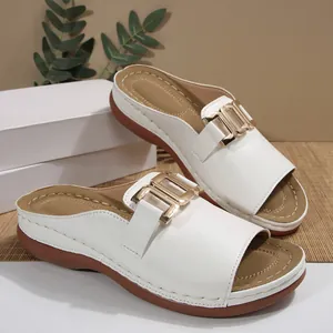 Close-up of white wedge slide sandals featuring a decorative gold-toned metal buckle.
