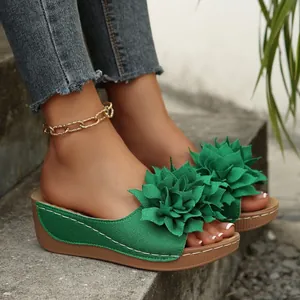 Gros plan de sandales compensées vertes ornées de grandes fleurs en tissu décoratives.
