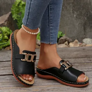 Close-up of black wedge slide sandals with decorative gold metal buckles and open toes.
