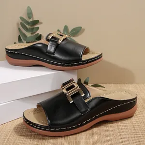 A detailed view showing the black leather-like upper and gold buckle on wedge sandals