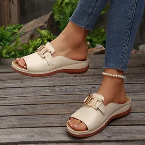 Detailed view of beige wedge sandals featuring a stylish gold metal buckle on a wooden deck.