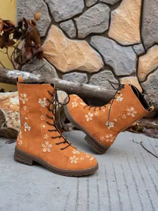 Detail view of orange suede mid-calf boots with delicate floral embroidery designs
