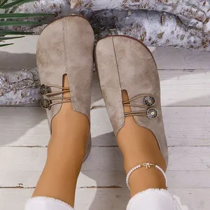 Primer plano de mocasines planos caqui casuales con botones decorativos y suela blanda.