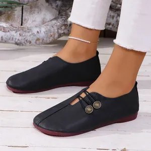 Primer plano de mocasines planos negros elegantes con punta redonda y dos botones decorativos.