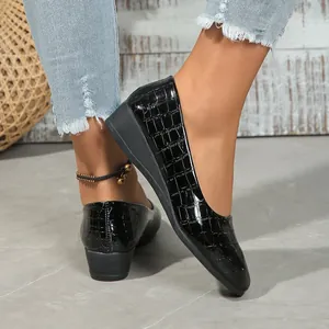Detailed view of chic black crocodile embossed pointed-toe wedge shoes on model's feet
