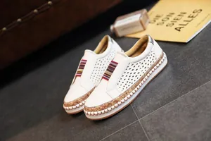 Détail de baskets en cuir perforé blanc avec une bande élastique rayée colorée.