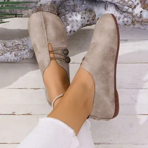 Primer plano de zapatos planos casuales beige con cierre de botón elástico.