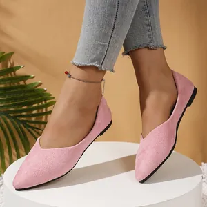 Detailed view of pink pointed-toe suede flats worn by a model in a studio setting.