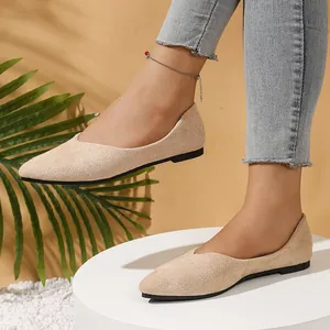 Close-up of beige suede pointed toe flats worn with jeans on a white pedestal.