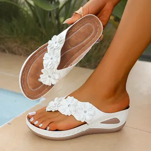 Detail view of white wedge platform flip-flops with delicate flower accents for women