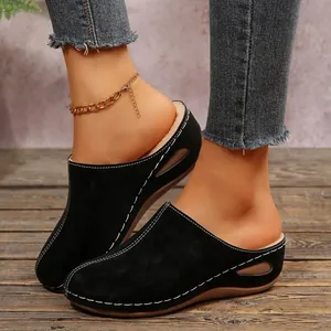 Close-up of black platform wedge mules with white stitching on rustic wood