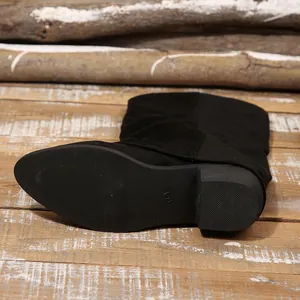 Detailed shot of vintage black suede tall boot sole and block heel on wood flooring