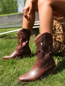 Close-up of vintage brown cutout western boots worn on a sunny grass background