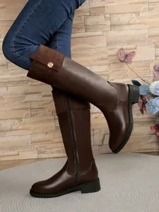 Side view of brown knee-high riding boots with suede patchwork and gold button detail