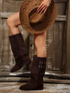 Detail of brown suede pant-leg boots with decorative double buckles and retro heel.