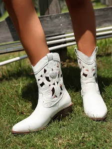 Detail of white western boots with intricate cutouts and chunky heels on grass.