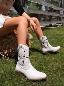 Detail of white retro western boots with hollow-out patterns worn outdoors on green grass