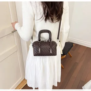 Model mit einer dunkelbraunen geflochtenen Boston-Tasche mit silbernen Details.