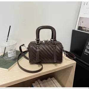 Detailansicht einer braunen gewebten Boston-Tasche mit silbernen Beschlägen auf Holz