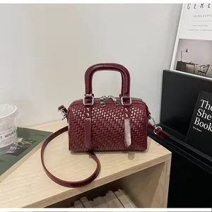 Nahaufnahme einer burgunderroten Boston-Tasche mit Webstruktur auf einem Holzregal