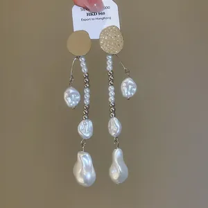 Gros plan de boucles d'oreilles vintage plissées en or avec de longues perles baroques.